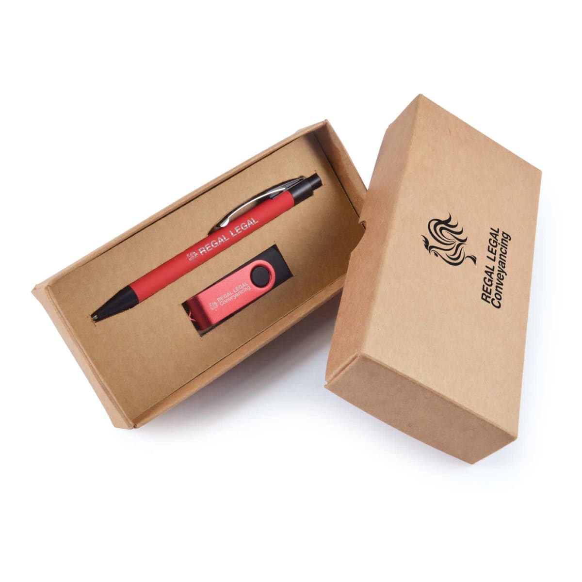 A red pen and keychain are placed in an open brown cardboard gift box. The pen displays REGAL LEGAL in white text, while the box lid shows the Regal Legal Conveyancing logo. The keychain matches the pens color and branding.