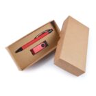 A red pen and a matching USB flash drive are neatly placed inside an open brown cardboard box, with the lid partially off to the side. The pen has a clip, and the USB drive features a swivel design.