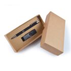 A black pen and USB flash drive set in a brown cardboard box, with the lid partially open. The pen has silver accents, and the flash drive is compact and black with a swivel cover. The box is plain and minimalist.