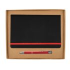 A cardboard box containing a black notebook with a red elastic band and a shiny red pen. The notebook and pen are neatly arranged, with the pen positioned horizontally below the notebook.