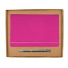 A closed pink notebook with an elastic band sits in a brown cardboard box. Below it is a silver pen positioned horizontally. The background is white.