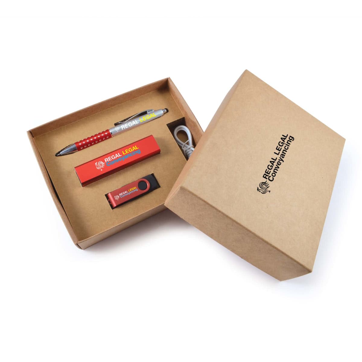 Open cardboard gift box with Regal Legal Consulting text on the lid. Inside are a branded pen, USB drive, and smartphone stand in red and black with company logos, along with a white charging cable.