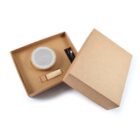 Open cardboard box showing a round, wooden Bluetooth speaker, charging cable, and a small rectangular wooden component on a white background.