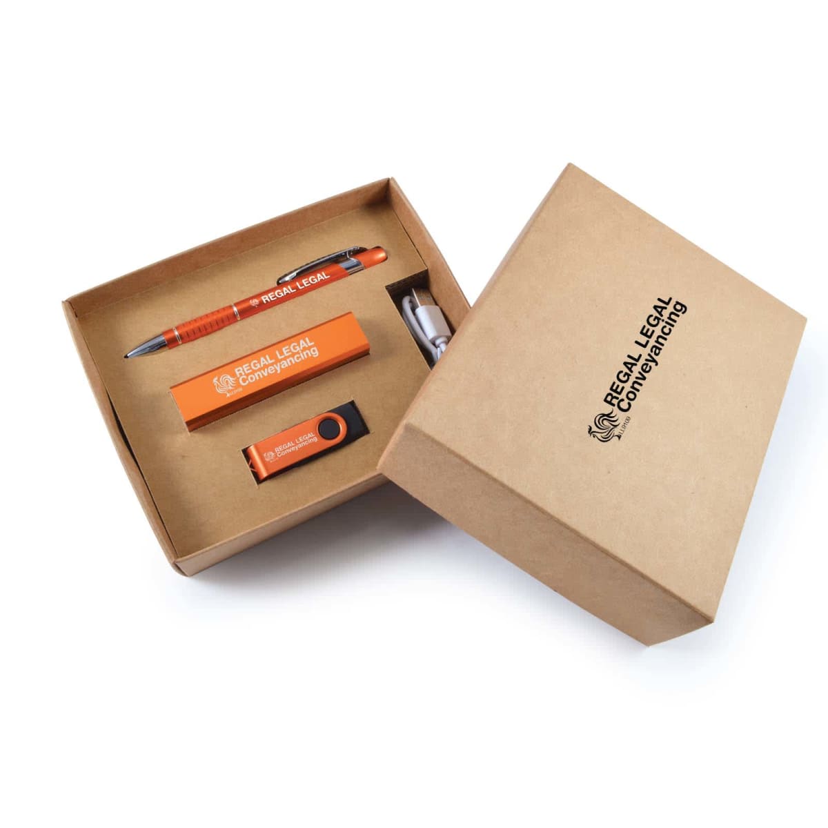 An open cardboard box displays branded merchandise, including an orange pen, a business card holder, a USB drive, and a silver keyring. The box and items are labeled Regal Legal Conveyancing.