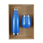 A blue insulated water bottle with a silver cap and a matching blue tumbler with a silver rim are placed inside a brown cardboard box.
