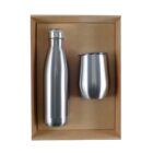 A stainless steel bottle and tumbler set inside a brown cardboard box with a clear lid. The bottle is tall with a screw-on cap, and the tumbler is slightly shorter and wider. Both have a brushed metal finish.