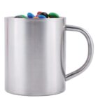 A silver metal mug filled with colorful candies, mostly in blue, red, green, yellow, and orange, with a smooth handle on the right side. The design is simple and glossy.