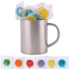 A metal mug filled with individually wrapped round candies in assorted colors: blue, yellow, and yellow-blue mix. Below the mug, six candies are aligned, showing additional orange, red, and green varieties, all in transparent wrappers.