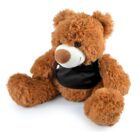 A fluffy brown teddy bear with a white snout and nose is sitting upright. It is wearing a small black vest, and its soft texture is visible. The bears round eyes give it a friendly appearance.