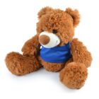 A fluffy brown teddy bear with a white snout is sitting upright. It is wearing a blue vest, and its legs are outstretched. The bear has a friendly expression and soft fur.