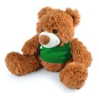 A fluffy brown teddy bear wearing a green vest sits facing slightly to the side. The bear has a white snout and dark eyes, with large plush limbs and a soft, cuddly appearance.
