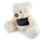 A fluffy white teddy bear with a large brown nose is seated with its arms outstretched. The teddy is wearing a black shirt and is positioned against a plain white background.