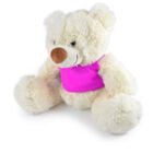 A fluffy white teddy bear wearing a bright pink shirt sits in a relaxed position with its legs spread out and arms resting on the ground. The bear has a light brown nose and a gentle smile.