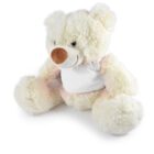 A fluffy, off-white teddy bear is sitting upright. It has a brown nose and is wearing a plain white T-shirt. The bear’s fur is soft and plush, with its arms and legs spread out slightly.