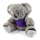 A plush koala toy wearing a purple shirt is sitting upright. The toy has soft, fuzzy gray fur, large round ears, and a friendly expression. Its paws are light gray, and its black eyes stand out on the fluffy face.