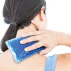 A woman with dark hair in a ponytail holds a blue gel pack against the back of her neck. She is wearing a light blue tank top and is positioned against a plain white background.