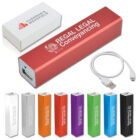 A collection of portable power banks in various colors including red, orange, green, purple, blue, white, black, and silver. The red one is labeled Regal Legal Conveyancing. A USB cable and a branded white box are also shown.