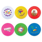 Six colorful frisbees with various logos: Kids Zone on white, Kanga Kampers on yellow, Chico Chicken on red, Vibes Music Fest on pink, VS Visual Systems on green, and Coco Island Beach Resort on blue.