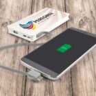 A smartphone is connected to a power bank via a gray cable on a wooden surface. The phone screen displays a full battery icon. The power bank has the Peregrini Financial logo and features USB ports.
