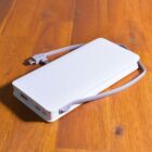 A white portable power bank with an attached charging cable rests on a wooden surface.