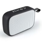 A portable black speaker with a white front grille. It has buttons on top for media controls, including play/pause, volume up, and volume down. A small black fabric loop is attached to one side for easy carrying.