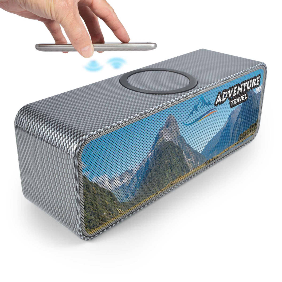 A wireless speaker with a mountainous landscape image on the front panel. A hand holds a smartphone above the speaker, indicating wireless connectivity. The speaker is labeled Adventure Travel.