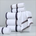 A stack of white towels with gray and black striped borders is neatly arranged on a white surface against a light gray background.