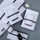 A collection of neatly folded white towels with gray and dark gray stripes, arranged on a gray surface. A black perfume bottle and a white soap in the shape of a shell are also present.