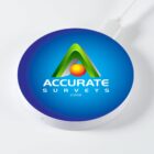 Round wireless charger with Accurate Surveys logo and green triangle design on blue background.