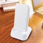 White wireless charger stand on a wooden table near a laptop.