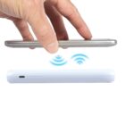 Hand holding phone over charging pad with wireless signal icons.