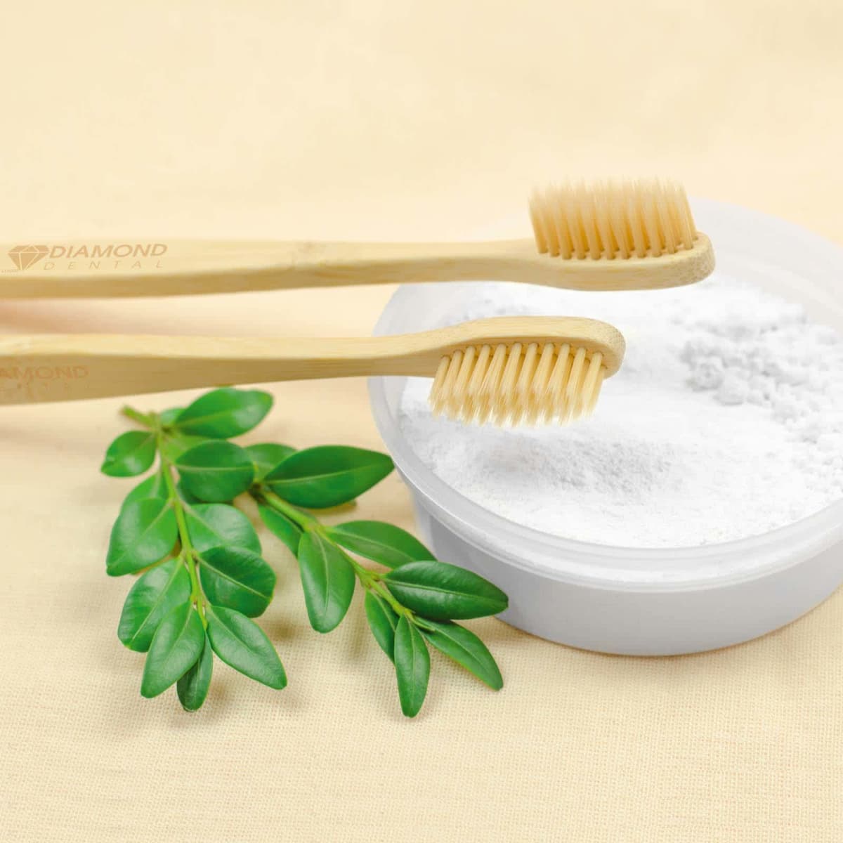 Bamboo toothbrushes with a round container of white powder and green leaves on a beige background.
