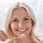 Smiling woman holding a toothbrush with toothpaste.