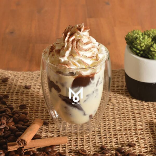 Glass with whipped cream dessert on a woven mat, surrounded by coffee beans and cinnamon sticks.