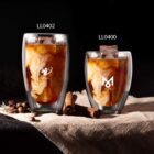 Two iced coffees with swirling cream in glass cups on burlap, surrounded by coffee beans and cinnamon.
