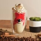 Glass with cream and strawberry sauce, surrounded by coffee beans and cinnamon sticks.