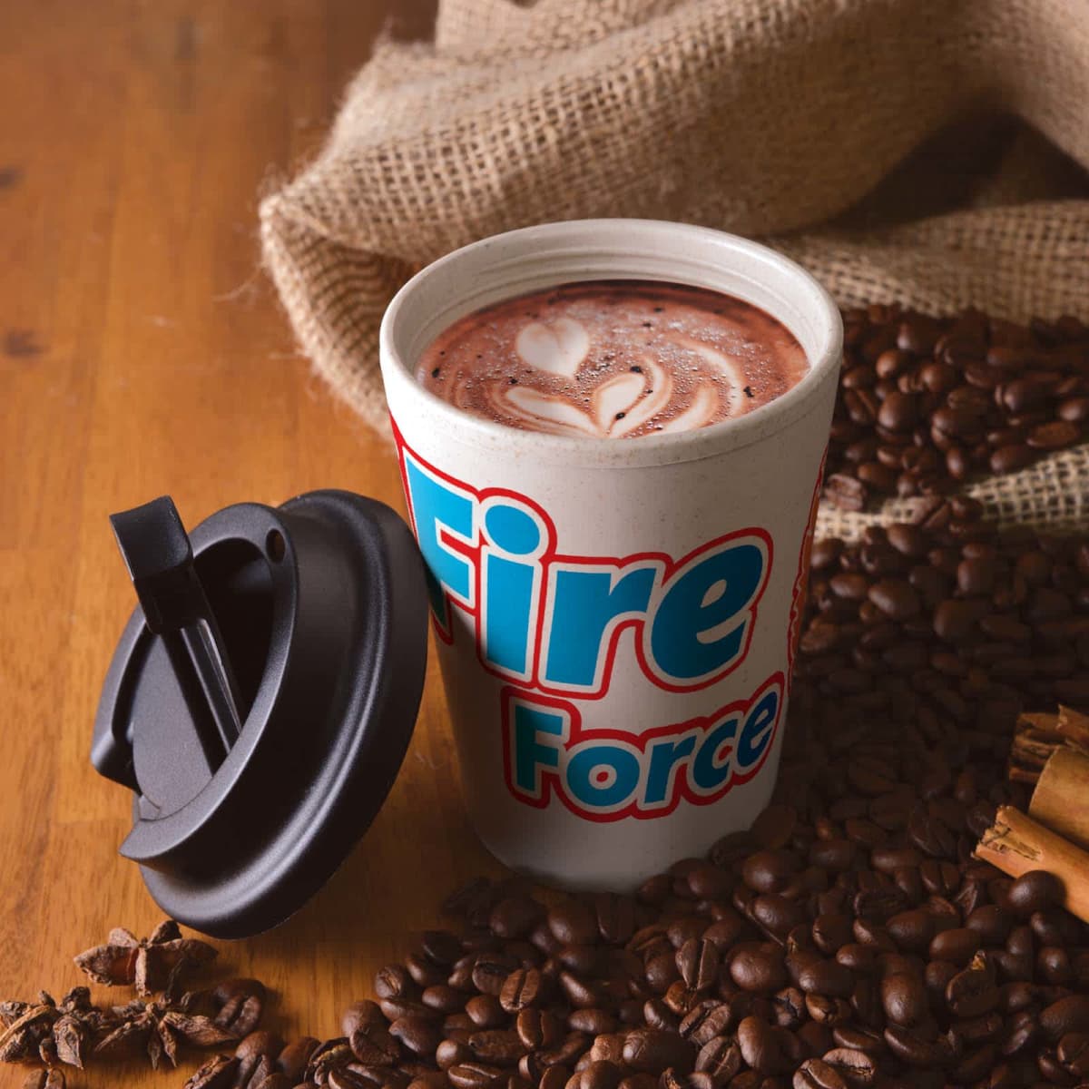 Cup of coffee with foam art next to its lid, surrounded by coffee beans on a wooden table.