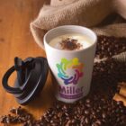 Coffee cup with foam and spice, surrounded by beans and burlap on a wooden table.