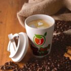 Coffee cup with latte art, lid off, surrounded by coffee beans on wooden table.