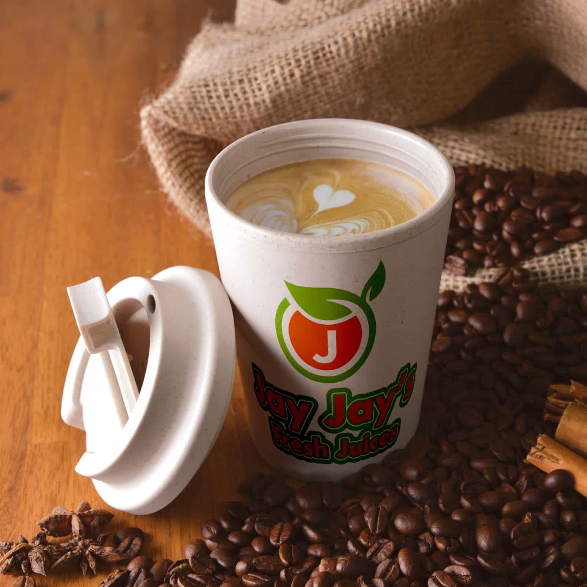 Coffee cup with latte art, lid off, surrounded by coffee beans on wooden table.