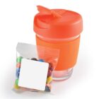 Orange travel mug with lid and a bag of colorful candies beside it.