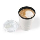 White travel mug with latte art next to a clear lid on a white background.