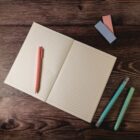 Open notebook with pens and sticky notes on a wooden table.