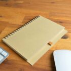 A spiral notebook on a wooden desk near a keyboard and mouse.