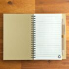 Open spiral notebook with lined pages and a pen on a wooden surface.
