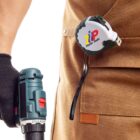 Person holding a power tool, wearing a tool belt with a measuring tape attached.