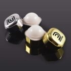 Two shiny earbud cases in silver and gold, with logo, on a reflective surface.