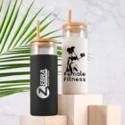 Two branded glass bottles with bamboo lids and straws, on wooden blocks. A green leaf in the background.