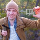 Person outdoors holding a multitool card, wearing a brown jacket and beanie, with trees in the background.