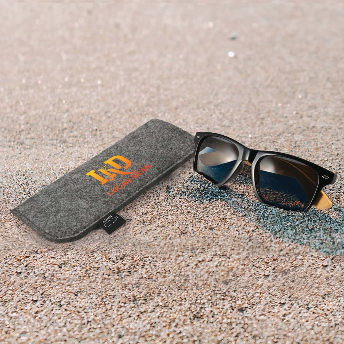 Sunglasses and a felt case on sandy ground.